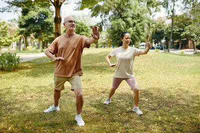 Du žmonės parke atlieka tai chi judesius, iškėlę rankas ir perkeldami kūno svorį.