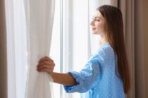 Moteris atitraukia užuolaidas prie šviesaus lango