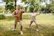Du žmonės parke atlieka tai chi judesius, iškėlę rankas ir perkeldami kūno svorį.